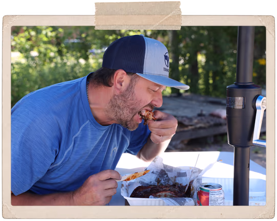 A customer digging into a box of smoked ribs at a picnic table